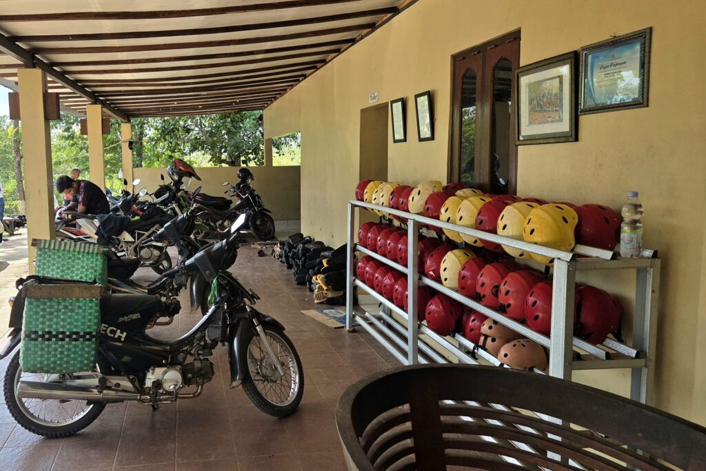 Regał z kaskami i zaparkowane motocykle w bazie przy Goa Jomblang