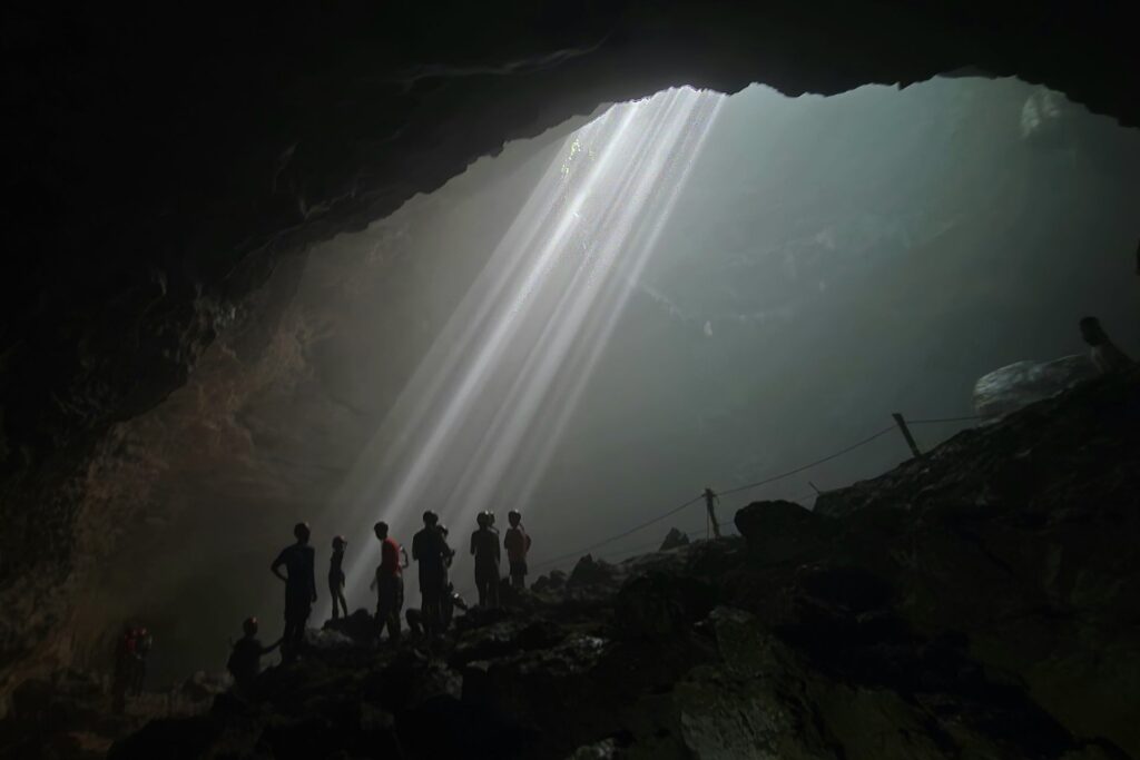 Grupa turystów na skałach pod snopami Heaven’s Light w Luweng Grubug